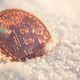 A coin with the bitcoin logo submerged in some snow.